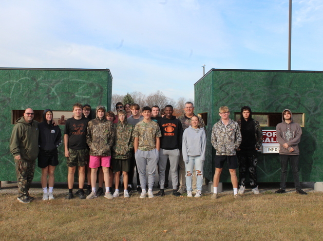 Students in building class stand in front of deer blinds.